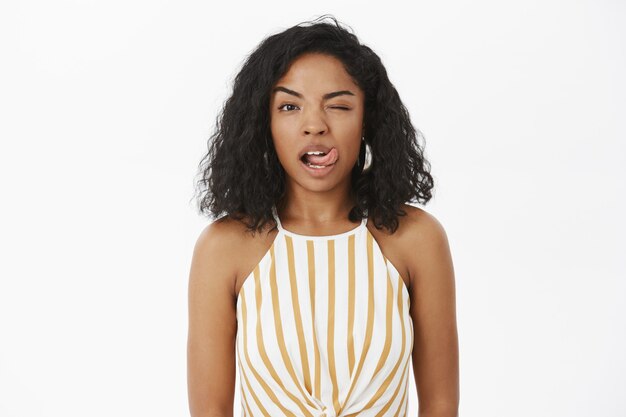 Mulher morena charmosa, atrevida e sensual, de pele escura, com blusa amarela listrada, piscando para fora