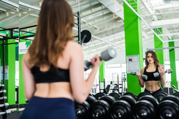 Foto grátis mulher morena com corpo forte ajuste está fazendo exercícios diferentes no sportclub moderno com espelhos