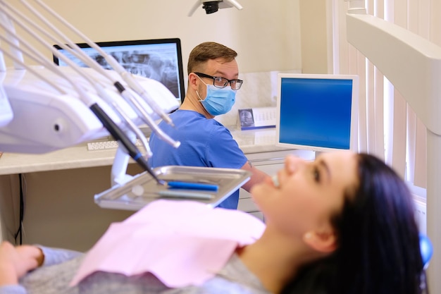 Mulher morena de beleza esperando enquanto dentista trabalhando em um computador. Visita de atendimento odontológico.