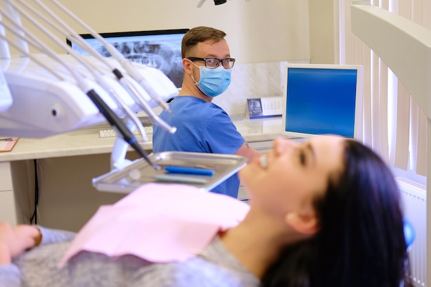 Mulher morena de beleza esperando enquanto dentista trabalhando em um computador. Visita de atendimento odontológico.