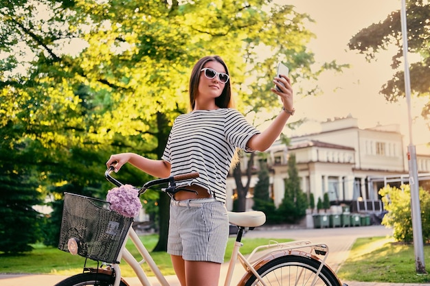 Mulher morena em um parque em uma bicicleta fazendo selfie com telefone inteligente.