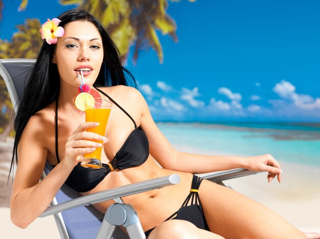 Mulher morena feliz de férias bebendo suco de laranja na praia