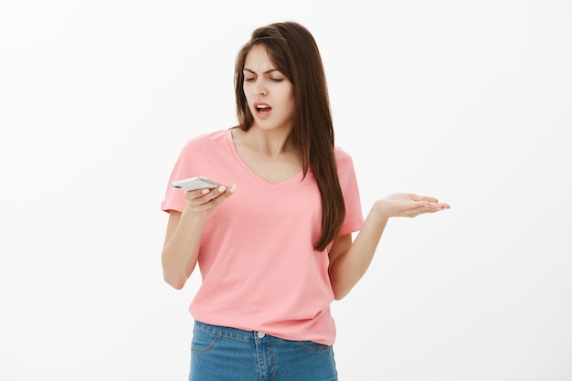 Mulher morena frustrada e incomodada posando no estúdio com seu telefone