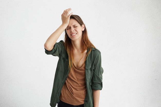 Foto grátis mulher morena frustrada, vestindo roupas casuais, segurando a mão na testa, sendo deprimida, lamentando o que ela fez com dor de cabeça. mulher confusa com rosto franzido e parecendo estressante e com alguma dor