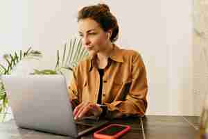 Foto grátis mulher morena muito alegre em fones de ouvido está trabalhando no laptop em coisas de trabalho ao redor da mesa humor alegre fazendo uma pausa trabalhando estudando relaxamento verdadeira emoção