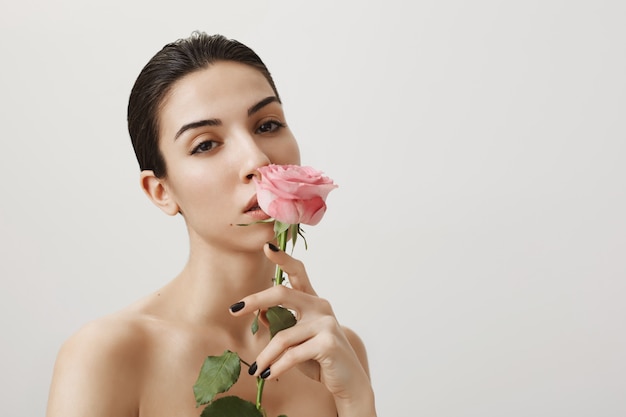 Mulher morena sensual com rosa nua olhando para a câmera cinza