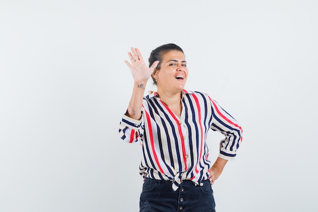 Mulher mostrando a palma da mão na camisa, saia e parecendo alegre.