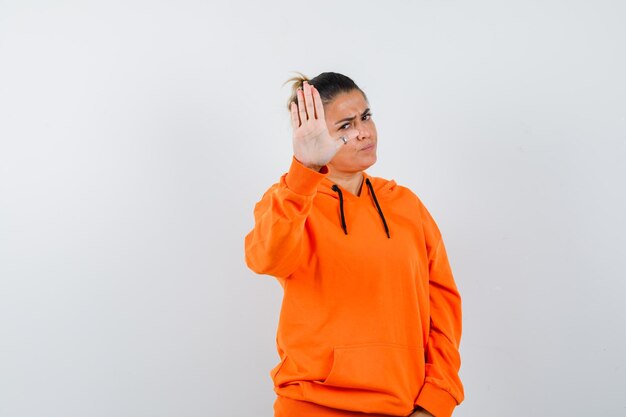 mulher mostrando gesto de parada com capuz laranja e olhando séria