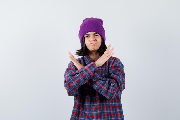 Mulher mostrando gesto de pare com camisa quadriculada e gorro, parecendo séria