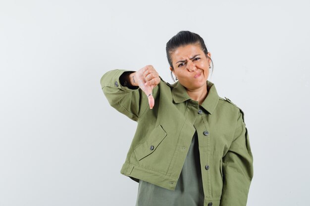 Mulher mostrando o polegar para baixo em jaqueta, camiseta e parecendo pensativa