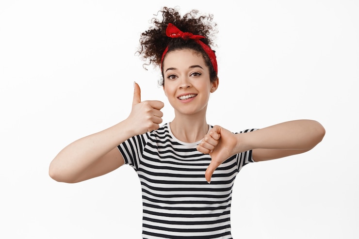 Foto grátis mulher mostrando os polegares para cima e para baixo, conceito de avaliação e feedback. em pé com tiara com cabelo cacheado penteado e camiseta branca