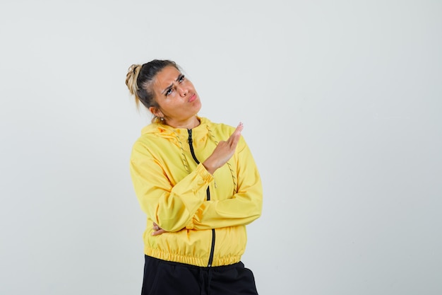 Mulher mostrando três dedos, mostrando a língua em um terno esporte e parecendo hesitante, vista frontal.