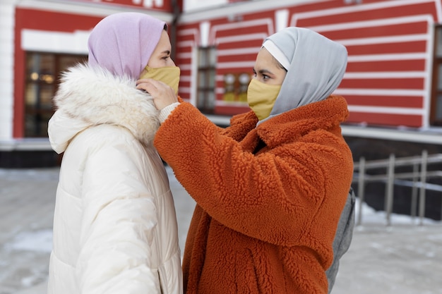Mulher muçulmana ajudando sua amiga a colocar uma máscara enquanto estava de férias