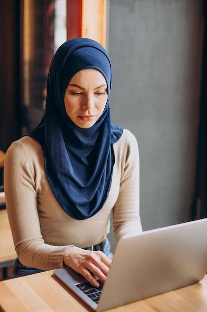 Mulher muçulmana moderna trabalhando em um laptop em um café