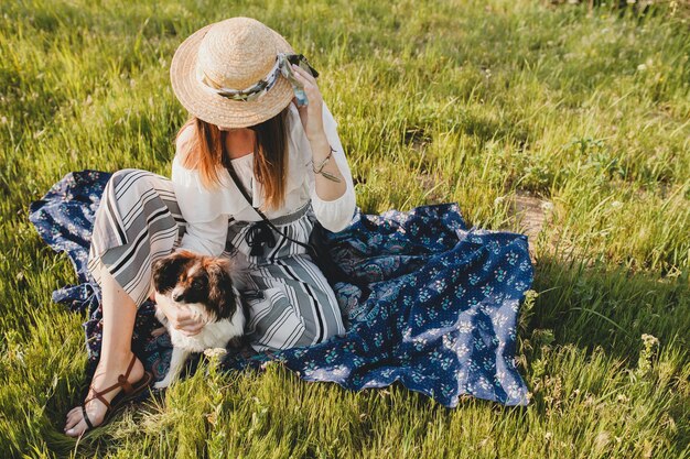 Mulher muito elegante no campo, segurando um cachorro, humor positivo e feliz, verão, chapéu de palha, roupa de estilo boêmio