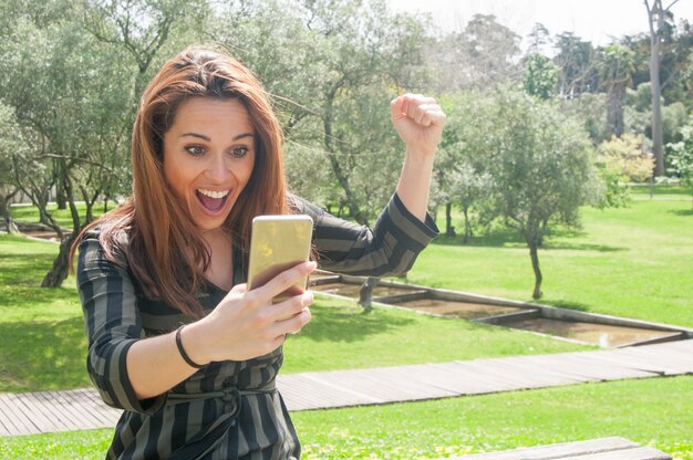 Mulher muito feliz com telefone móvel, comemorando a vitória