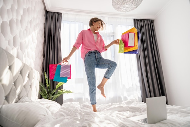 Foto grátis mulher muito feliz pulando na cama em casa fazendo compras online