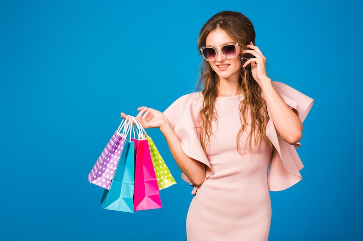 Foto grátis mulher muito jovem e elegante em um vestido rosa luxuoso, usando um telefone celular e segurando sacolas de compras