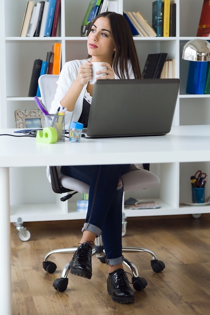 Mulher muito jovem trabalhando com laptop em seu escritório.