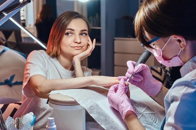 Mulher muito sonhadora com tatuagem recebeu cuidados com as unhas de uma jovem manicure diligente.