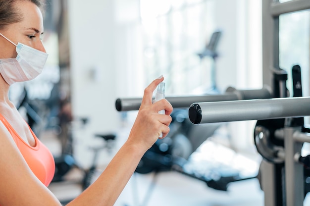 Mulher na academia com máscara médica, desinfetando equipamentos de ginástica