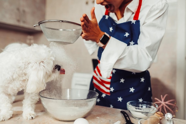 Mulher na cozinha peneira farinha junto com um cachorro