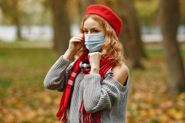 Mulher na floresta de outono. Pessoa com máscara. Tema Coronavirus. Senhora em um lenço vermelho.