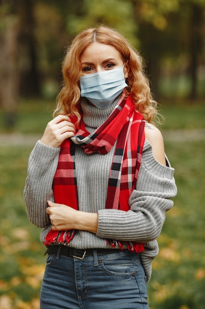 Mulher na floresta de outono. pessoa com máscara. tema coronavirus. senhora em um lenço vermelho.