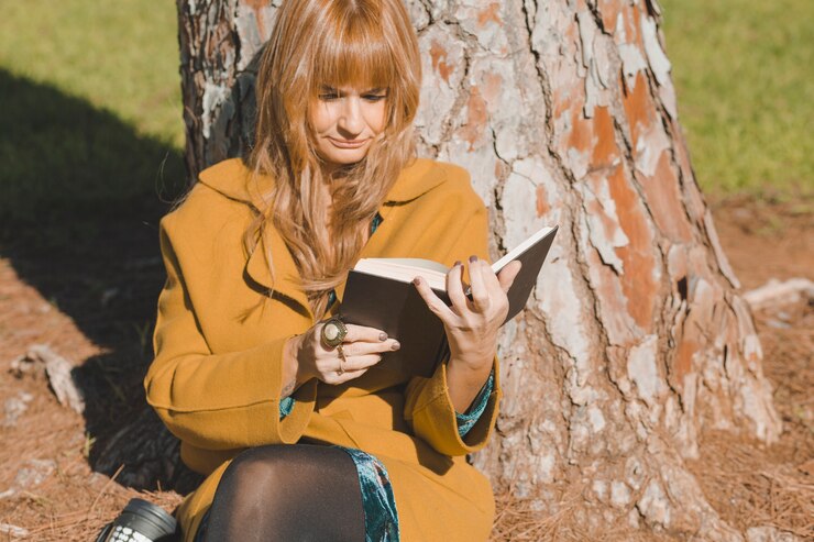 Foto grátis mulher na leitura do casaco debaixo da árvore