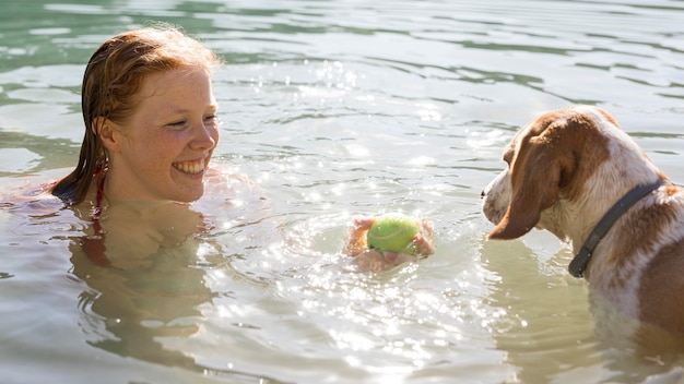 Mulher nadando e brincando com um cachorro ao sol