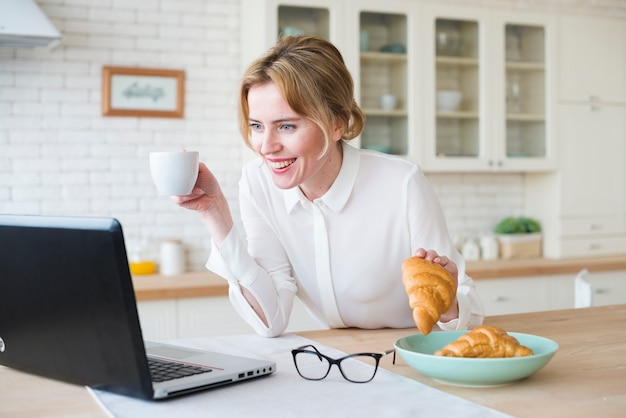 Mulher negócio, com, croissant, usando computador portátil