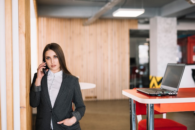 Mulher negócio, falando por telefone, em, parede, em, escritório