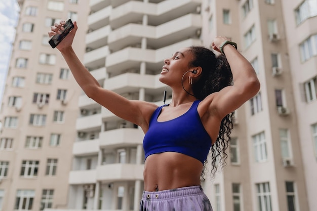 Foto grátis mulher negra afro-americana atraente em roupa de ginástica esportiva no telhado fazendo exercícios