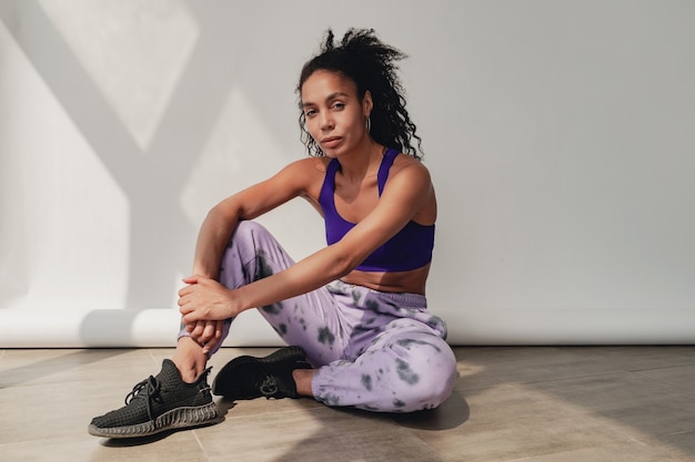 mulher negra afro-americana sentada em um elegante hippie fitness fitness top violeta e calça branca
