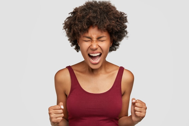 Mulher negra agressiva com corte de cabelo afro, fecha os punhos com raiva, sente-se louca e desesperada, dá as mãos na frente, pronta para a luta ou o desafio