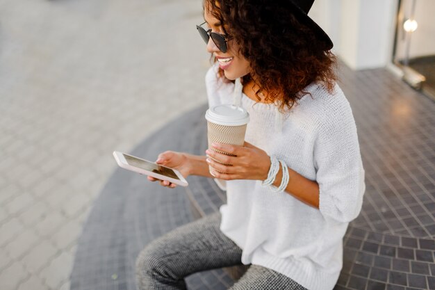 Mulher negra bem sucedida, blogueiro ou gerente de loja, usando telefone celular durante o coffee-break.