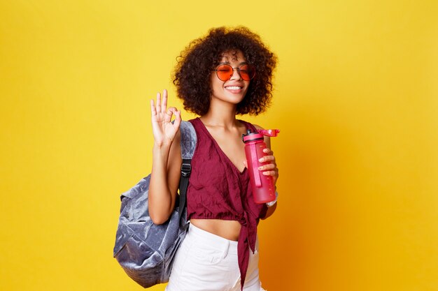 Mulher negra brincalhona feliz com roupa de verão elegante e o símbolo da paz posando em amarelo