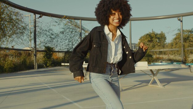 Mulher negra com enorme cabelo afro e roupas estilo disco dançando ao ar livre na zona do parque de tênis