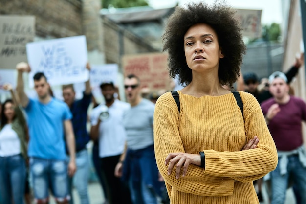 Mulher negra confiante com braços cruzados em frente a multidão de pessoas durante manifestações pelos direitos civis negros