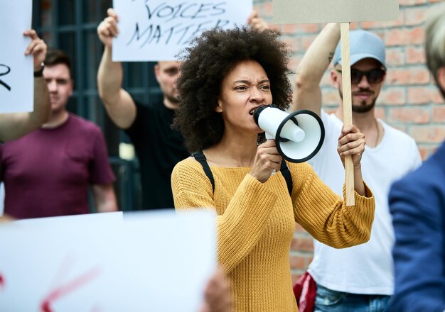 Mulher negra descontente participando de manifestações anti-racismo e gritando pelo megafone