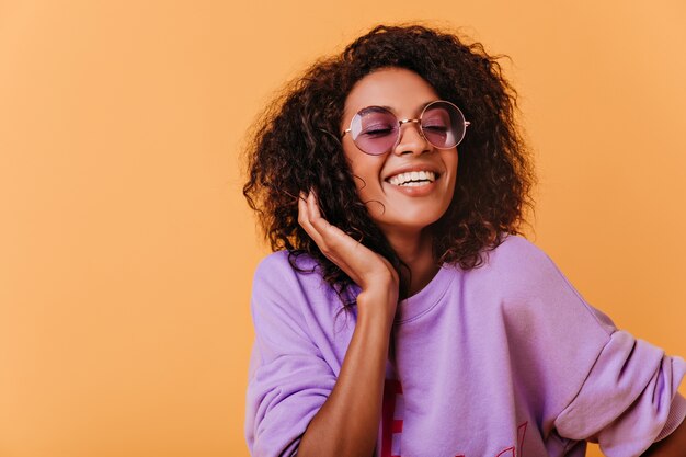 Mulher negra elegante posando em colorido com um sorriso alegre. Garota africana otimista com suéter roxo