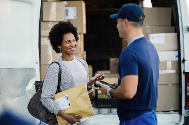 Mulher negra feliz se comunicando com um mensageiro enquanto entrega seu pacote