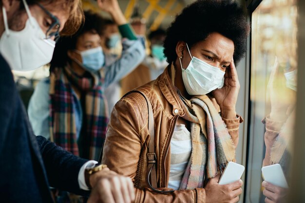 Mulher negra preocupada usando máscara facial enquanto viaja de transporte público durante a pandemia de coronavírus