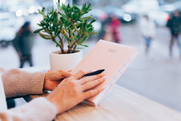 Mulher no café, perto da parede de vidro, segurando o bloco de notas do caderno de papel, sinal 2021