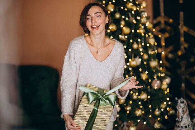Mulher no Natal, segurando um presente de Natal pela árvore de Natal