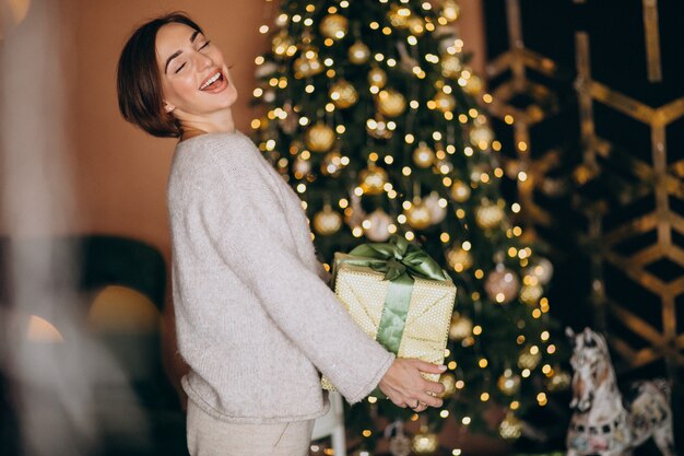 Mulher no Natal, segurando um presente de Natal pela árvore de Natal
