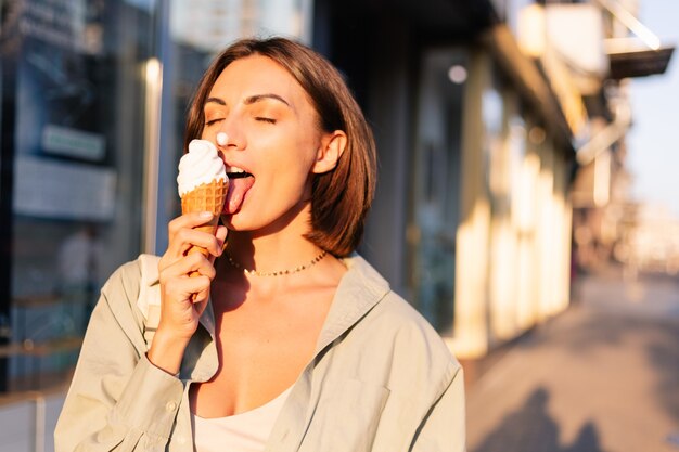 Mulher no pôr do sol de verão tomando sorvete na rua da cidade