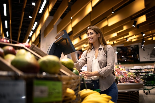 Mulher no supermercado usando balança digital self-service para medir o peso da fruta
