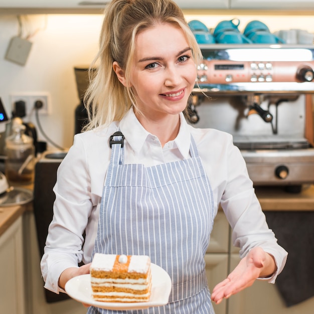 Foto grátis mulher nova de sorriso que apresenta a fatia do bolo na cafetaria