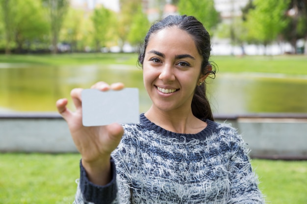 Mulher nova de sorriso que mostra o cartão em branco no parque da cidade